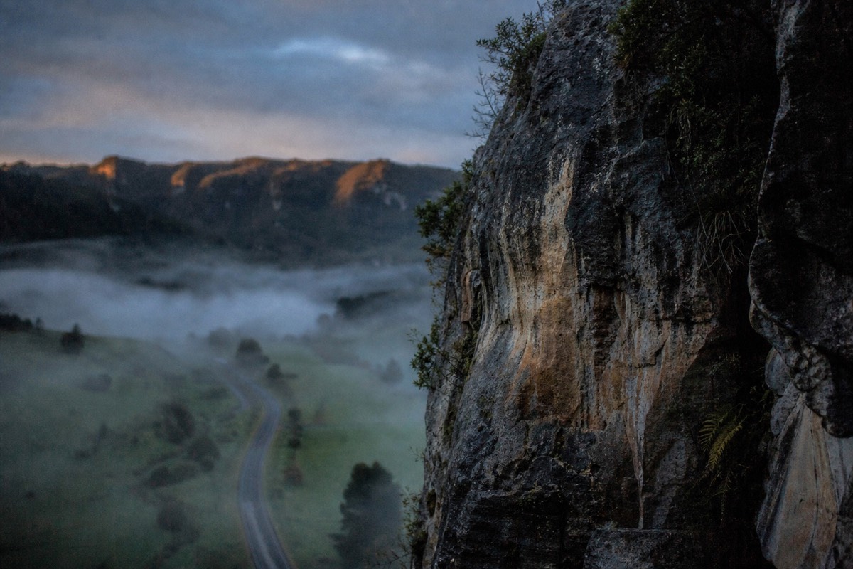 Morning mist lying in a green Waikato valley with limestone outcrops breaking through and sun catching the top of the ridge