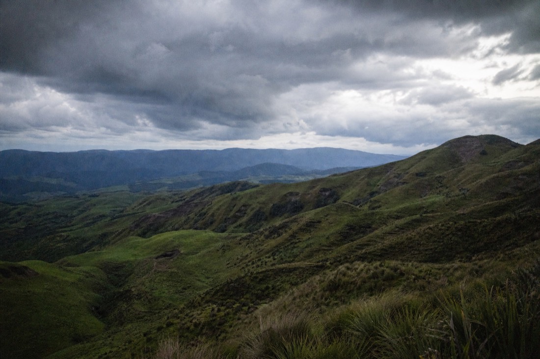 Another view at Waitomo: a wide New Zealand North Island landscape of green volcanic hill country rolling away to a distant blue ridge under big weather