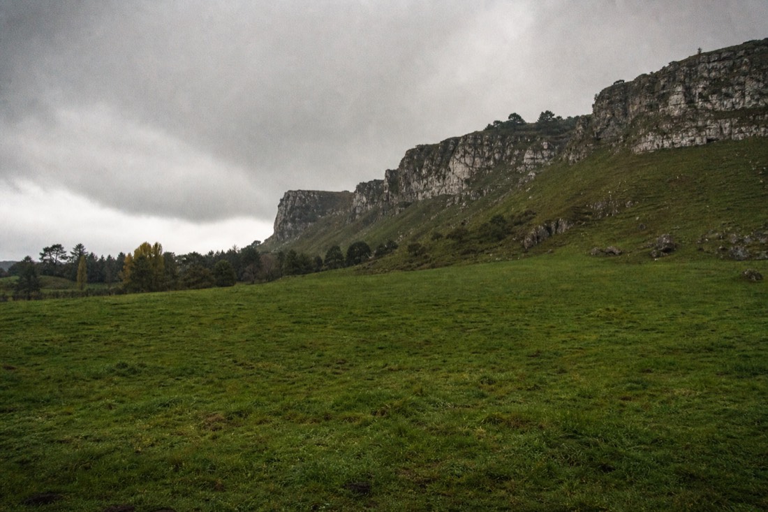 Another view at Waitomo: green Waikato hill country with limestone outcrops under a shifting sky, half sunlit and half under a rain squall