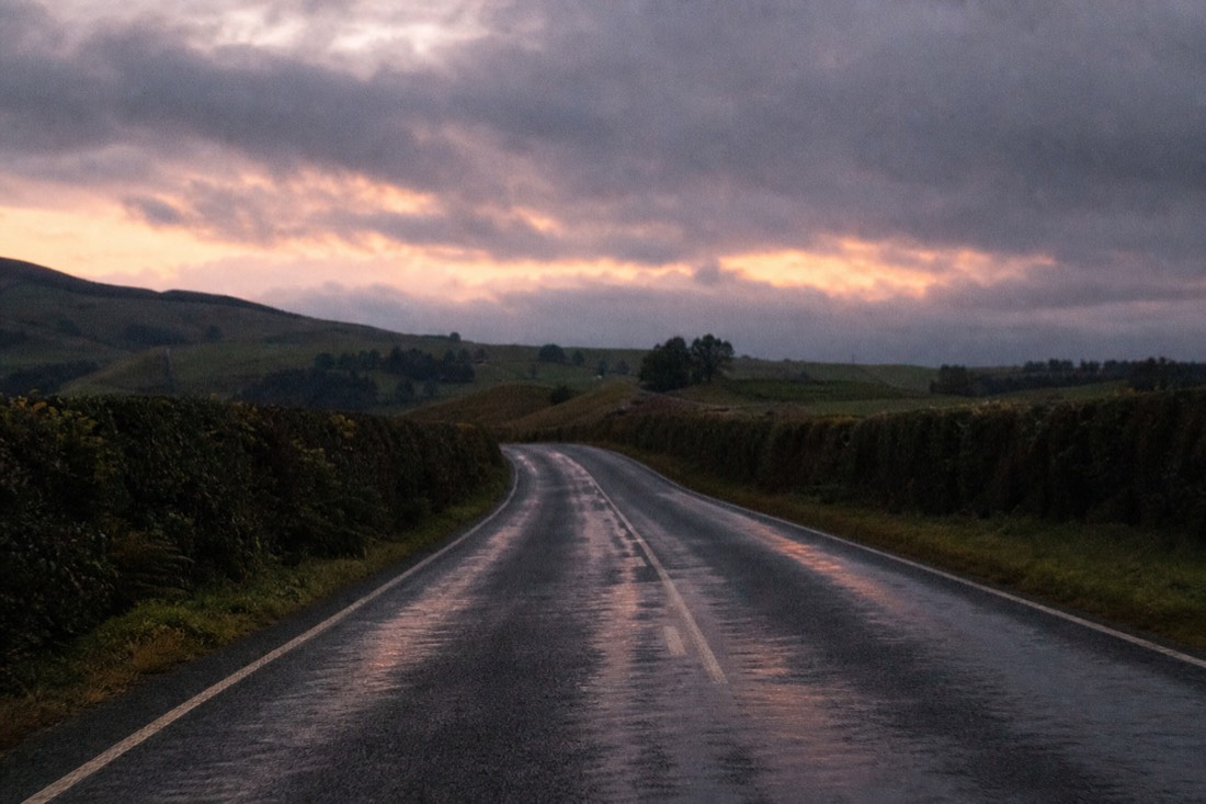Another view at Waitomo: a two-lane New Zealand state highway running through rolling green farmland towards distant limestone hills under low cloud